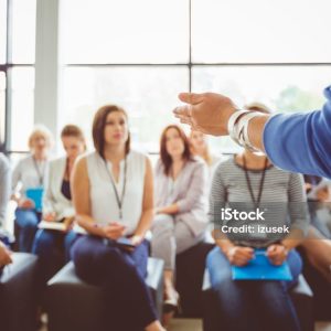 Hand of a trainer addressing group of females sitting in a conference hall. Female hand against defocused group of women attending seminar.
